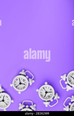A pattern of many white classic alarm clocks in the form of a pattern on a purple background. Top view with a copy of the space, flat lay. Concept of Stock Photo