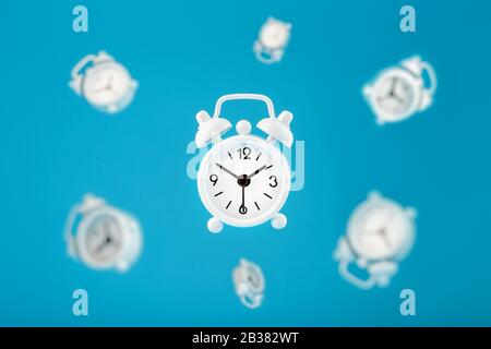 White retro alarm clocks in flight in the center, isolated on a blue background.Creative modern still life concept of flying time. Levitation Stock Photo