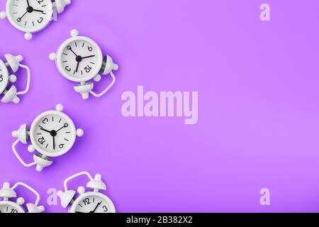 A pattern of many white classic alarm clocks in the form of a pattern on a purple background. Top view with a copy of the space, flat lay. Concept of Stock Photo