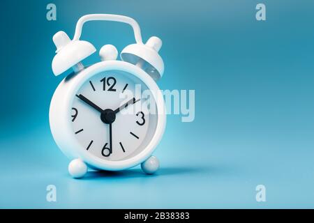 White retro alarm clock on blue background. Concept of time with free space for text. Minimal style Stock Photo