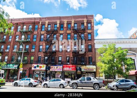 New York City, USA - August 4, 2018: Street with old typical apartment buildings with its fire escape and people around in the Harlem neighborhood in Stock Photo