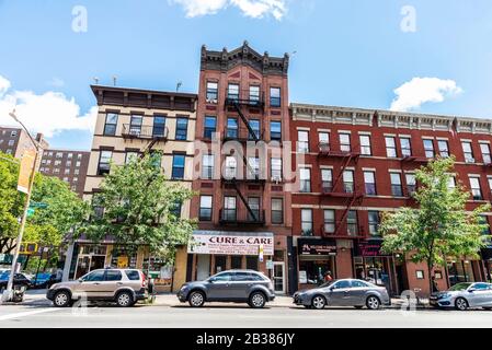 New York City, USA - August 4, 2018: Street with old typical apartment buildings with its fire escape and people around in the Harlem neighborhood in Stock Photo