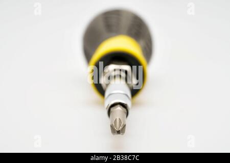 Close up selective focus of a screw driver with a black and yellow handle pointing at the camera on a white isolated background Stock Photo