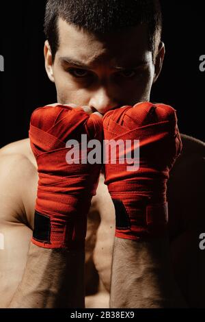 Boxer male fighter posing in confident defensive stance with hands in banndages up on black background Stock Photo