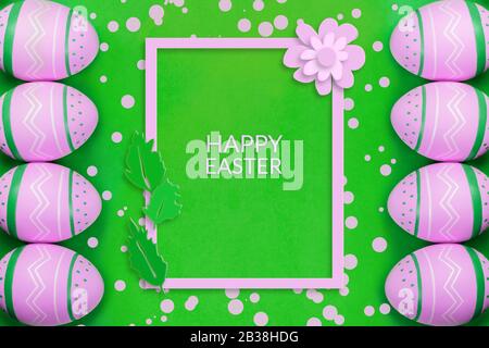 Colored decorated eggs on the bright green background with pink confetti and frame with paper cut out flower and leaves and sign Happy Easter. Easter concept, card Stock Photo