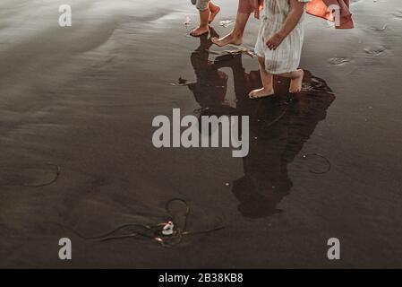 Reflection in ocean water of mother walking two daughters at beach Stock Photo