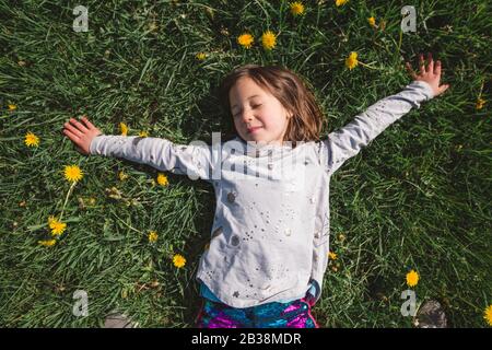 A happy child lays down in a field of wildflowers with closed eyes Stock Photo