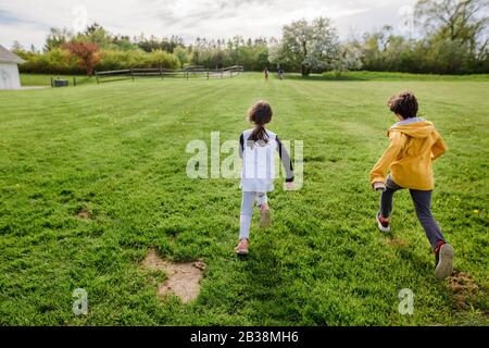 Three children run through a field at springtime, one far ahead