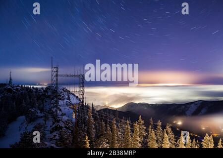 Communication towers, power lines, star trails, and low clouds lit by city lights from the Squaw Mountain Lookout, Arapaho National Forest, Colorado. Stock Photo