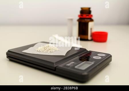 The laboratory scale of black color on table with material on surface and opened bottle near. Stock Photo