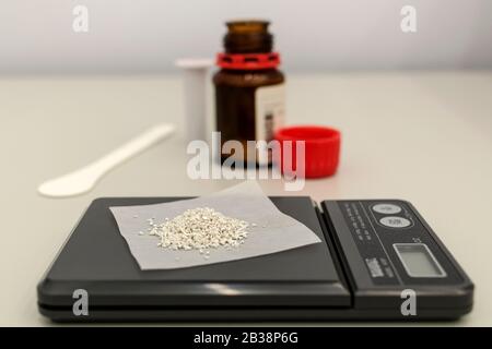 The laboratory scale of black color on table with material on surface and opened bottle near. Stock Photo