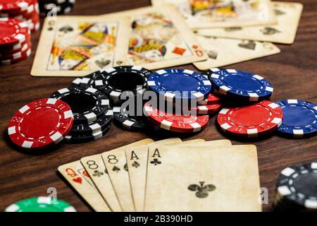 Dead Mans Hand against a pair of queens, vintage used cards and poker chips in blue, red, green and Black on a wood table with soft warm color toning. Stock Photo