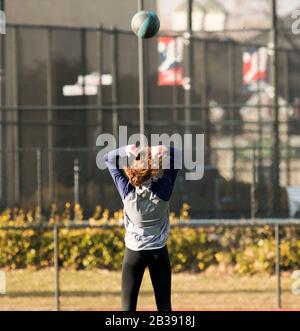 Female high school track and field athlete throwing a medicine ball backwards Stock Photo