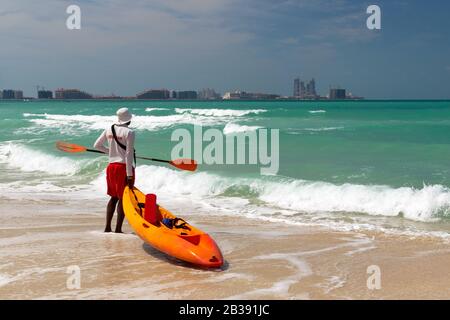 Lifeguard on duty seen from behind with orange boat and paddle in hand. Stock Photo