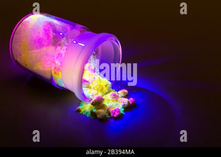 Fluorescent organic materials of red, yellow and green color for production OLED inside glass bottle in UV light. Stock Photo