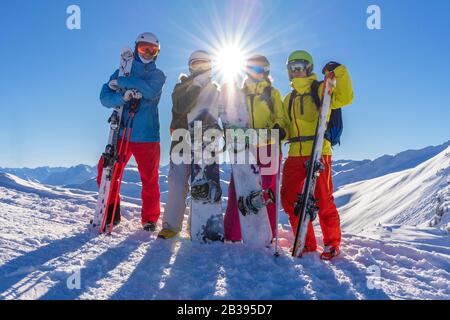Four happy friends snowboarders and skiers are having fun on ski slope with ski and snowboards in sunny day. Stock Photo