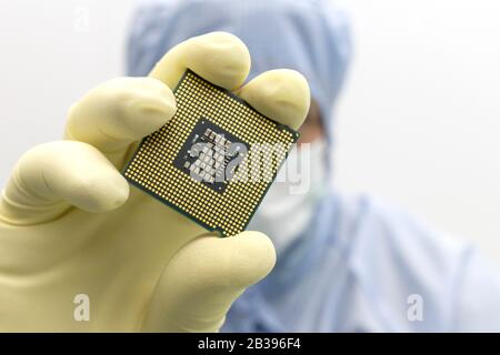 An engineer working in a clear room wearing a special uniform and protective glasses holds processor cpu in hands in glove Stock Photo
