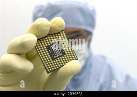 An engineer working in a clear room wearing a special uniform and protective glasses holds processor cpu in hand in glove Stock Photo