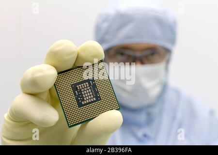 An engineer working in a clear room wearing a special uniform and protective glasses holds processor cpu in hand in glove Stock Photo