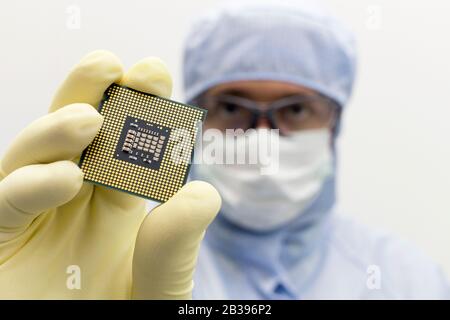 An engineer working in a clear room wearing a special uniform and protective glasses holds processor cpu in hand in glove Stock Photo