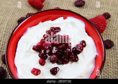 Healthy detox diet snack: Close up of isolated red bowl with pomegranate seeds and white yoghurt Stock Photo