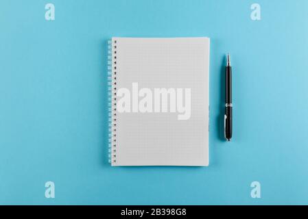 top view of squared spiral notepad and ballpoint pen on blue background Stock Photo