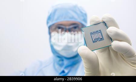 An engineer working in a clear room wearing a special uniform and protective glasses hold processor cpu by hand in glove Stock Photo
