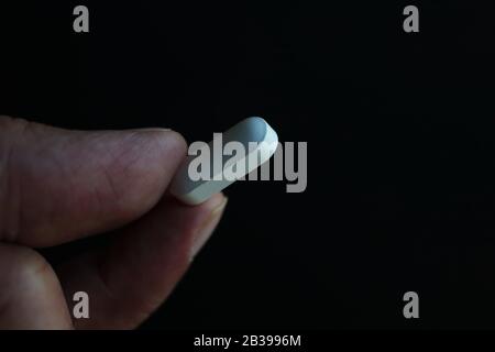 White pill held between fingers Stock Photo
