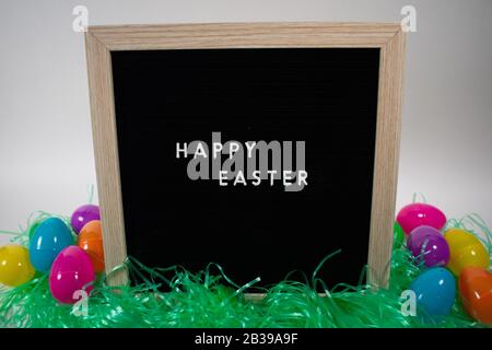 A Black Happy Easter Sign With White Letters, Easter Grass, and Easter Eggs Stock Photo