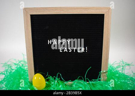 A Black Happy Easter Sign With White Letters, Easter Grass, and Easter Eggs Stock Photo