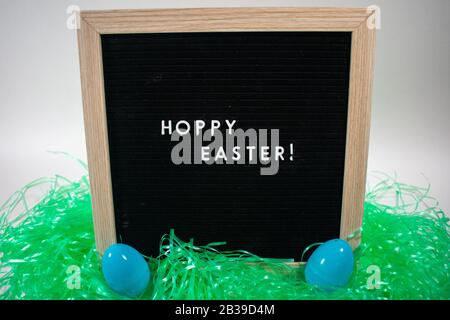 A Black Happy Easter Sign With White Letters, Easter Grass, and Easter Eggs Stock Photo