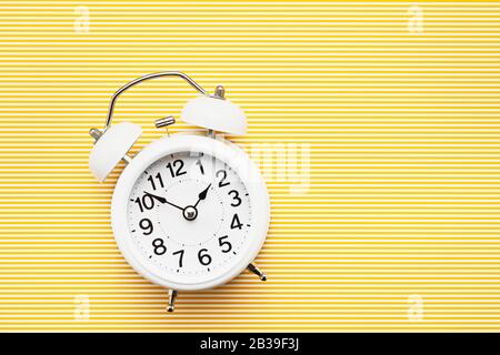 White vintage alarm clock on yellow background. Top view, copy space. Daylight saving concept.