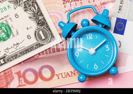 The alarm clock lies on various money, a view from above. Concept Time - Money Stock Photo