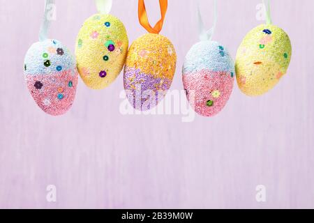Hanging Easter eggs decorated in various colors. Festive background with copy space Stock Photo