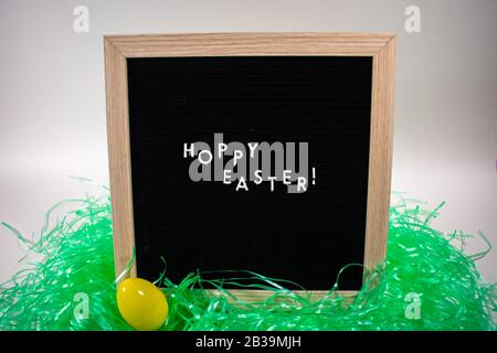 A Black Happy Easter Sign With White Letters, Easter Grass, and Easter Eggs Stock Photo