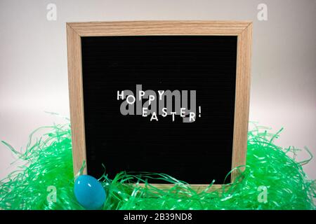 A Black Happy Easter Sign With White Letters, Easter Grass, and Easter Eggs Stock Photo