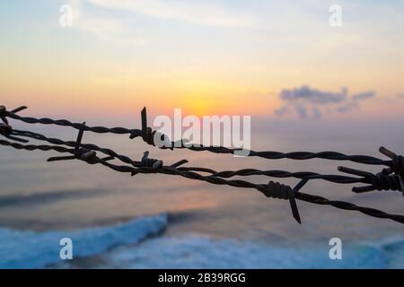 Barbed wire fence against sunset sky and sea. Stock Photo