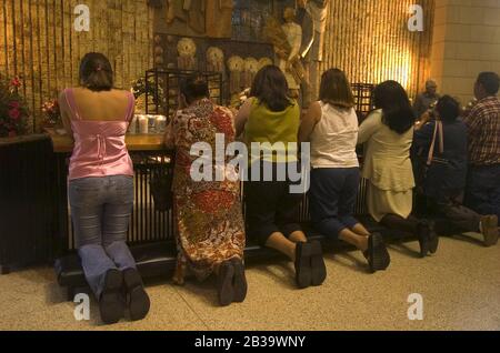 San Juan Texas USA, circa 2004: Mourners kneel and pray in front of an array of votive candles in the Basilica of Our Lady of Del Valle. ©Bob Daemmrich Stock Photo