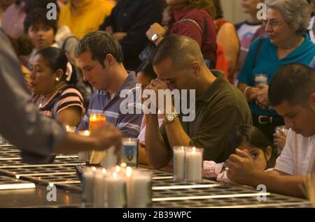 San Juan Texas USA, circa 2004: Mourners kneel and pray in front of an array of votive candles in the Basilica of Our Lady of Del Valle. ©Bob Daemmrich Stock Photo