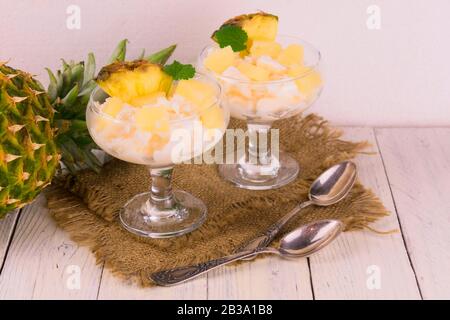 Two servings of frozen yogurt with slices of pineapple on a white wooden background. Stock Photo
