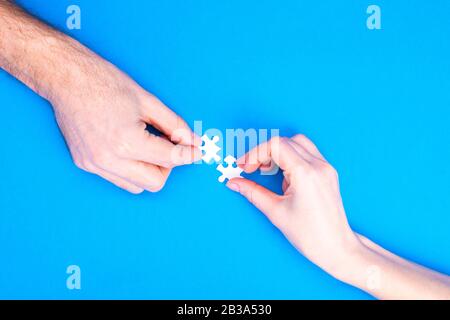 Hands of man and woman collect puzzles on a blue background background. Conceptual image of joint cooperation in the family. View from above Stock Photo