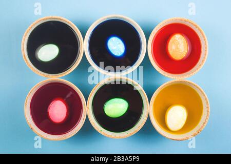 Eggs are painted in different colors in colored water with dyes in six bowls.. Minimalistic Easter layout. Stock Photo