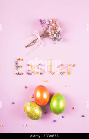 Easter creative layout with the word Easter made of flowers, a bouquet of small flowers and cute eggs on the lilac background. Stock Photo