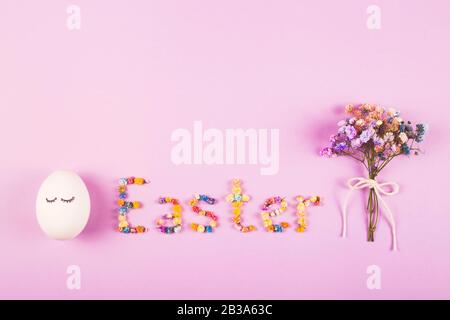 Easter creative layout with the word Easter made of flowers, a bouquet of small flowers and cute eggs on the lilac background. Stock Photo