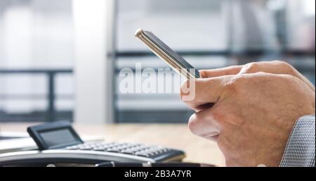 Businessman hands typing on smartphone at office desk. Extreme closeup Stock Photo