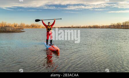 senior male paddler in a drysuit and life jacket is paddling a long racing stand up paddleboard on a lake in Colorado, winter or early spring scenery, Stock Photo