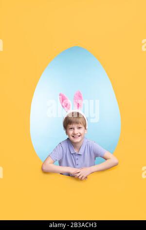 Portrait of happy excited boy in ear hare headband standing in Easter egg-shaped frame Stock Photo