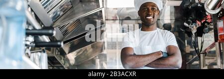 panoramic shot of positive african american chef standing with crossed arms in food truck Stock Photo