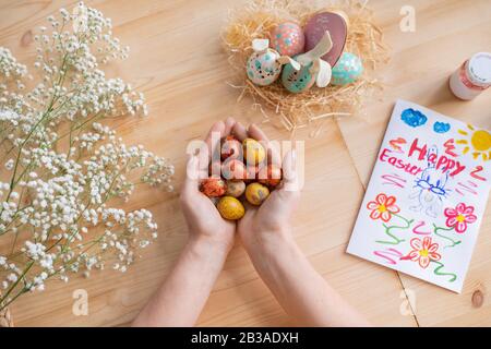 Above view of unrecognizable woman holding painted quails eggs above wooden table with Easter card and babys breath Stock Photo
