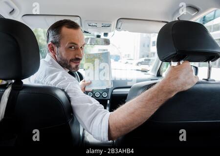 selective focus of bearded man sitting in car and holding map Stock Photo